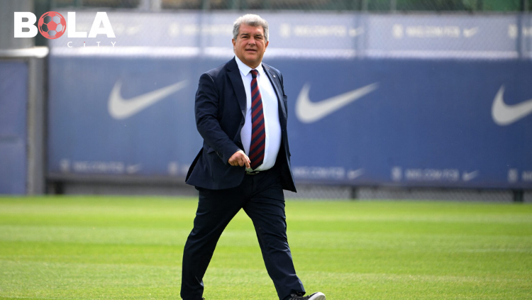 Joan Laporta berjalan di lapangan latihan FC Barcelona dengan mengenakan jas biru dan dasi merah biru di kompleks latihan klub.